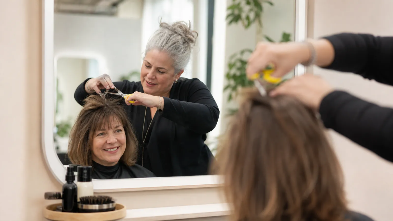 Hair stylist cutting a client's hair in a salon mirror with yellow-handled shears
