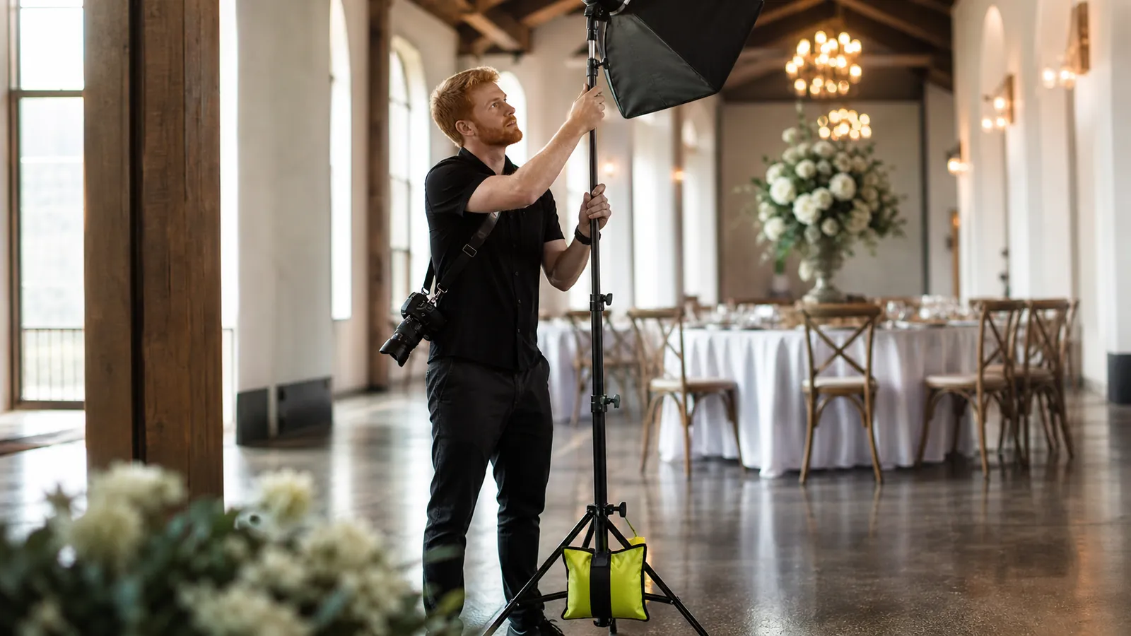 Photographer steadying a light stand anchored by a yellow sandbag inside a wedding venue